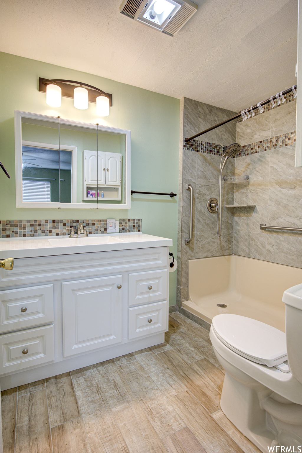 Bathroom featuring toilet, tiled shower, a textured ceiling, and oversized vanity