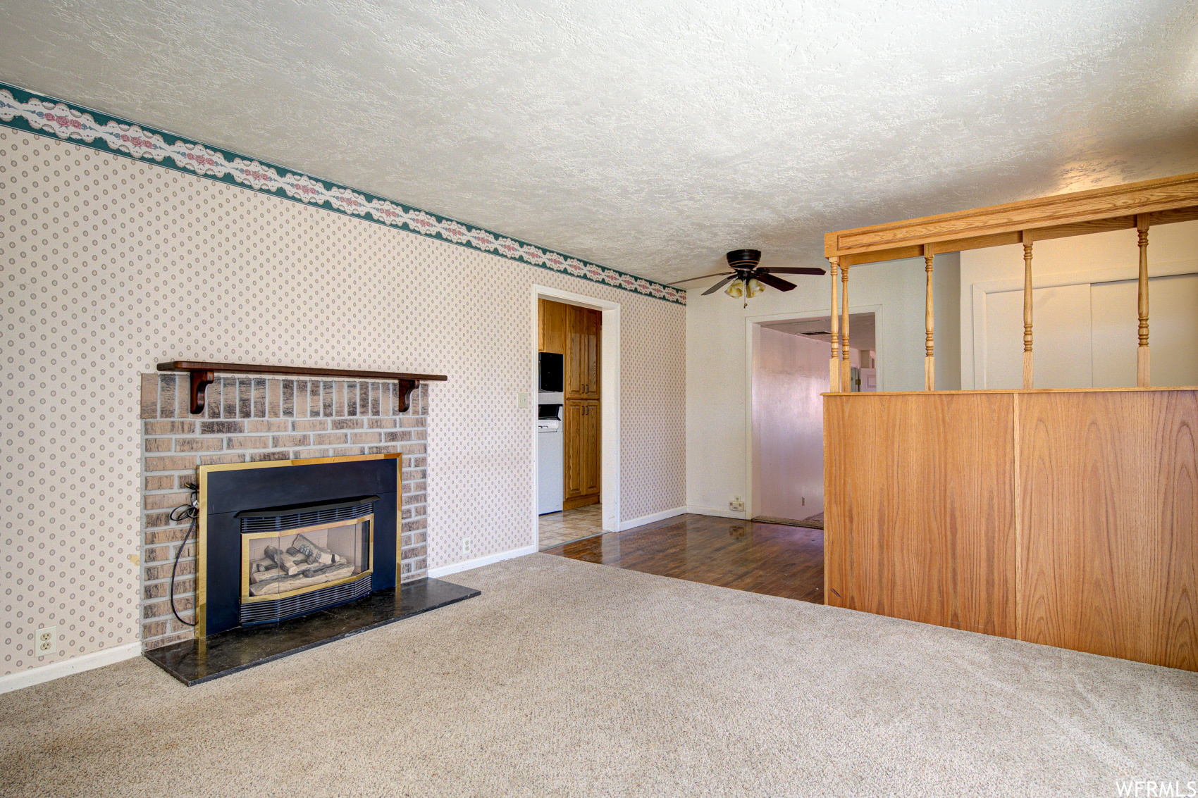 Unfurnished living room featuring a brick fireplace, ceiling fan, carpet floors, and a textured ceiling