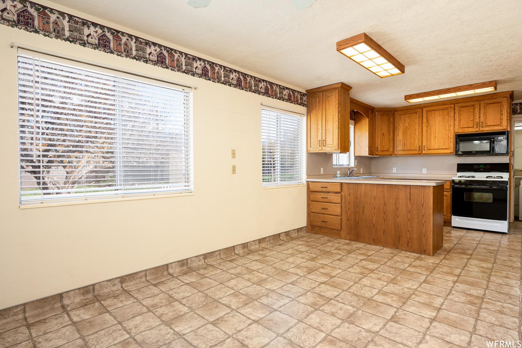 Kitchen with white range, light tile flooring, sink, and kitchen peninsula