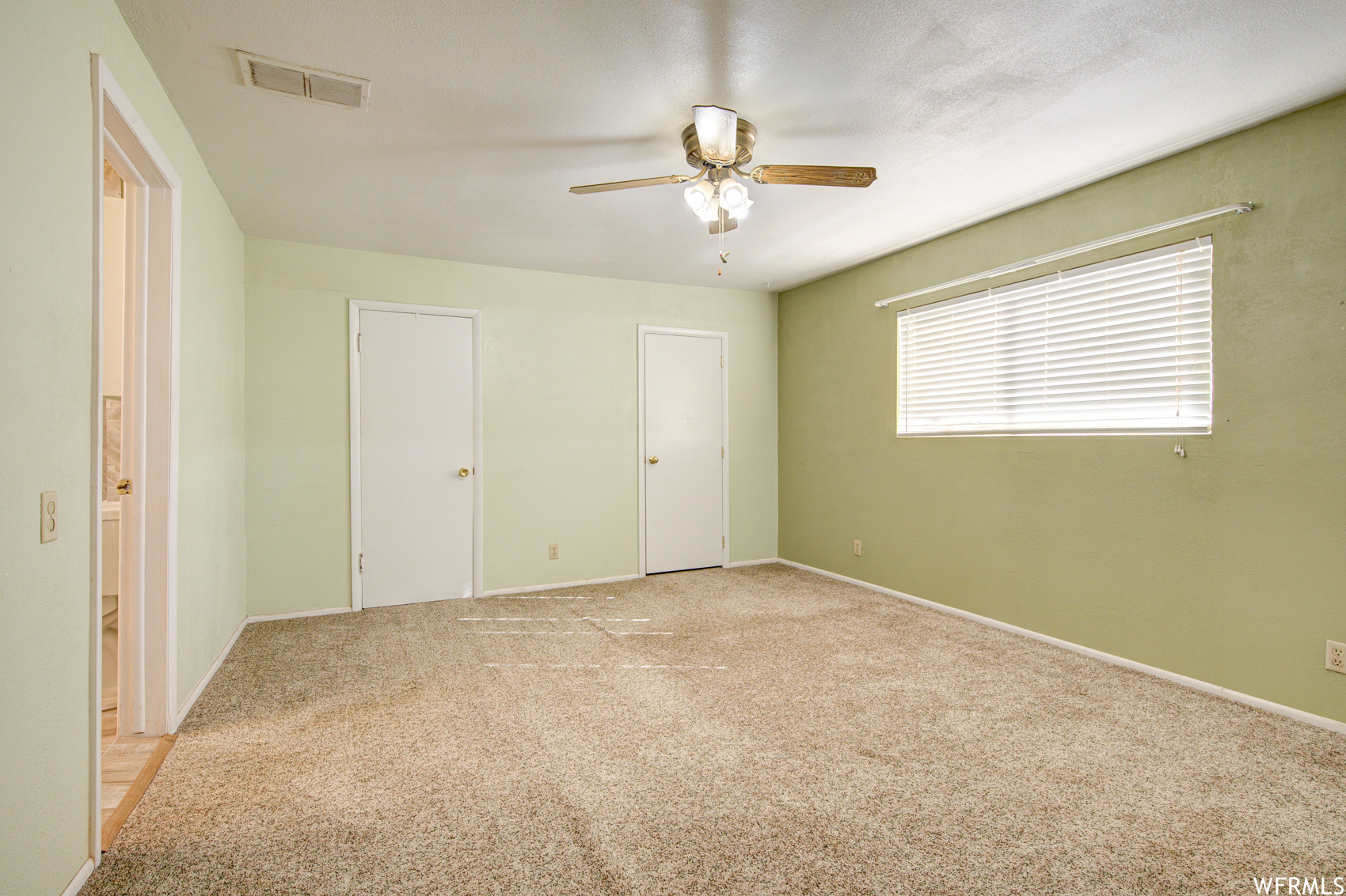 Unfurnished bedroom featuring light carpet, multiple closets, and ceiling fan