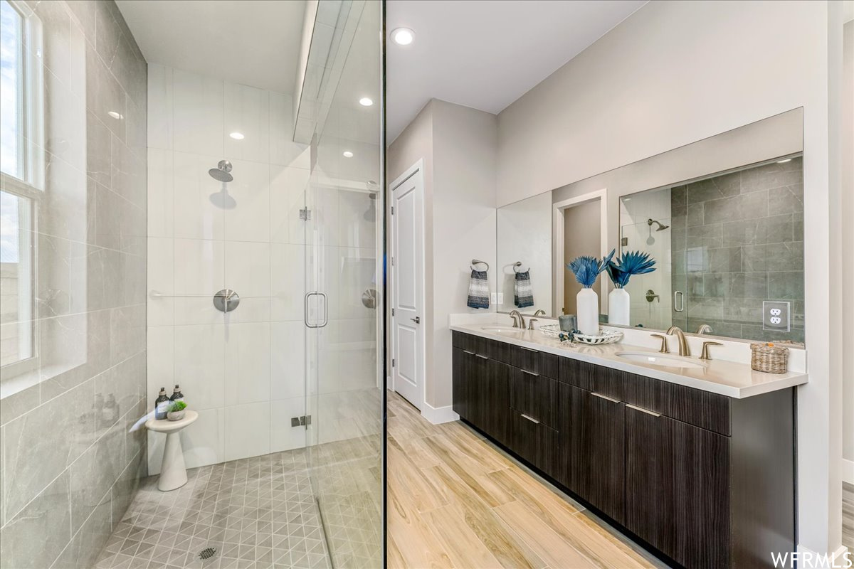 Bathroom featuring tile walls, dual bowl vanity, a shower with shower door, and hardwood / wood-style flooring