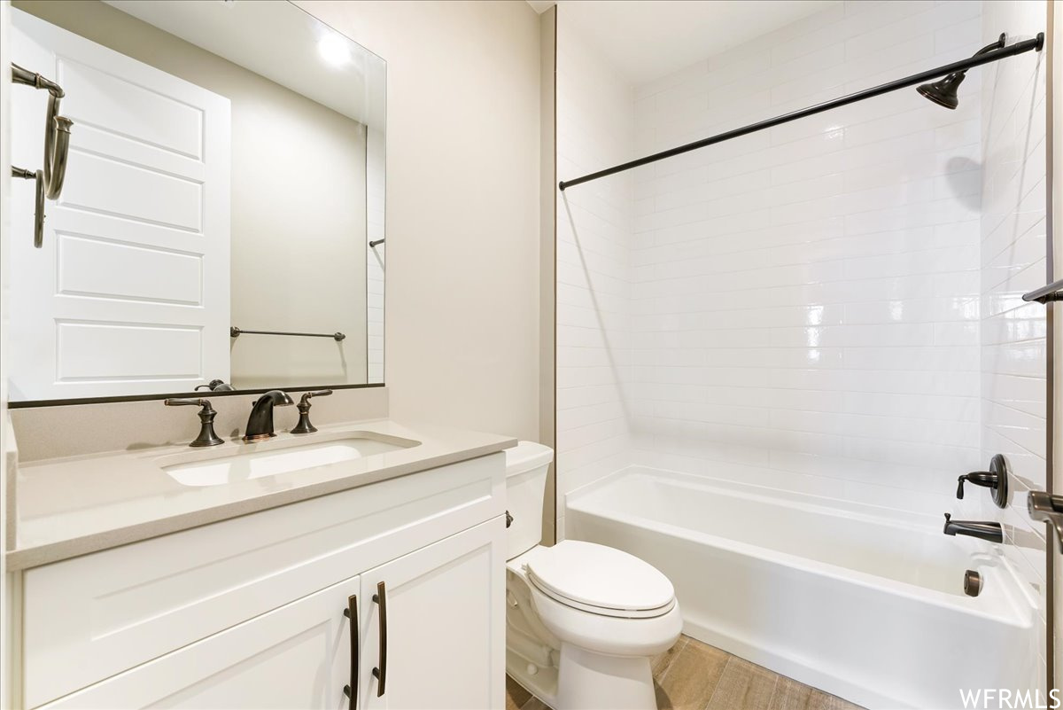 Full bathroom featuring toilet, tiled shower / bath combo, oversized vanity, and hardwood / wood-style floors