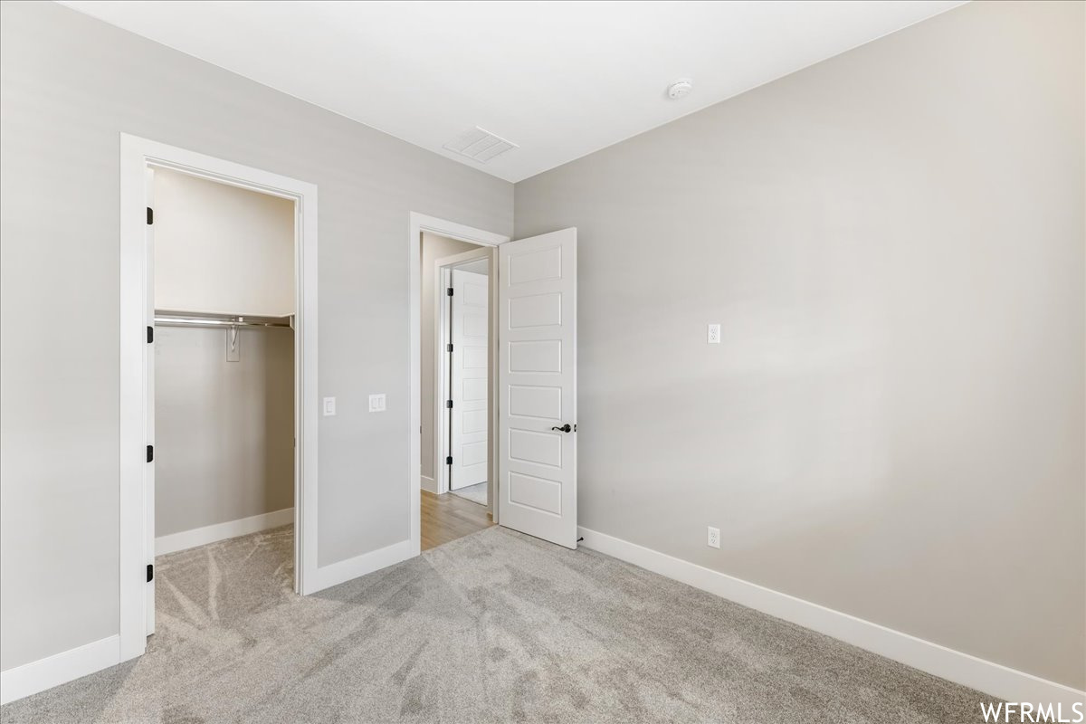 Unfurnished bedroom with a walk in closet, a closet, and light colored carpet