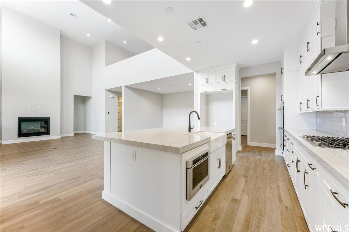 Kitchen featuring a kitchen island with sink, appliances with stainless steel finishes, white cabinetry, and light hardwood / wood-style floors