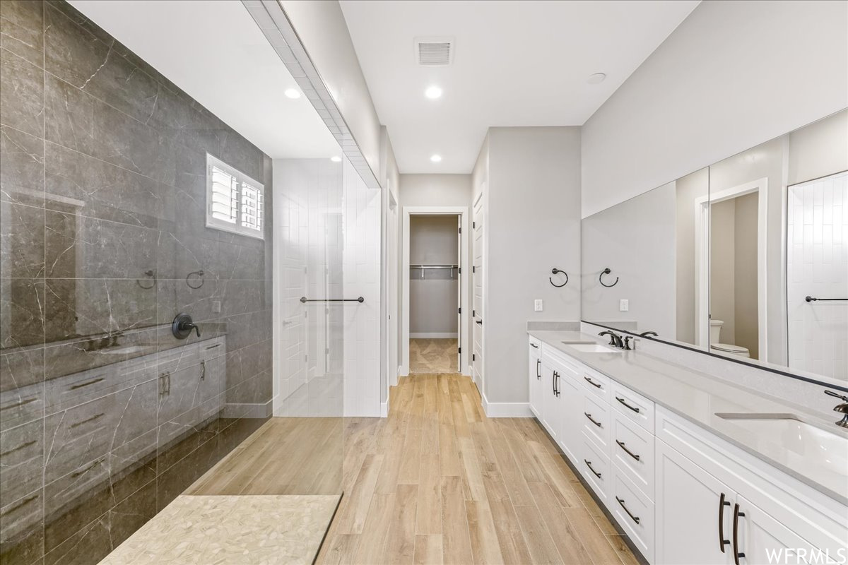 Bathroom featuring toilet, oversized vanity, hardwood / wood-style flooring, double sink, and tiled shower