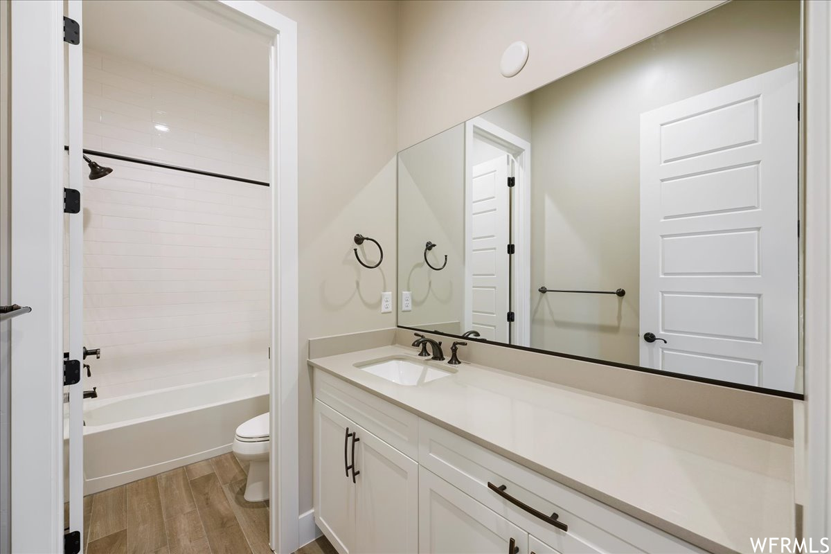 Full bathroom featuring oversized vanity, shower / bathing tub combination, wood-type flooring, and toilet