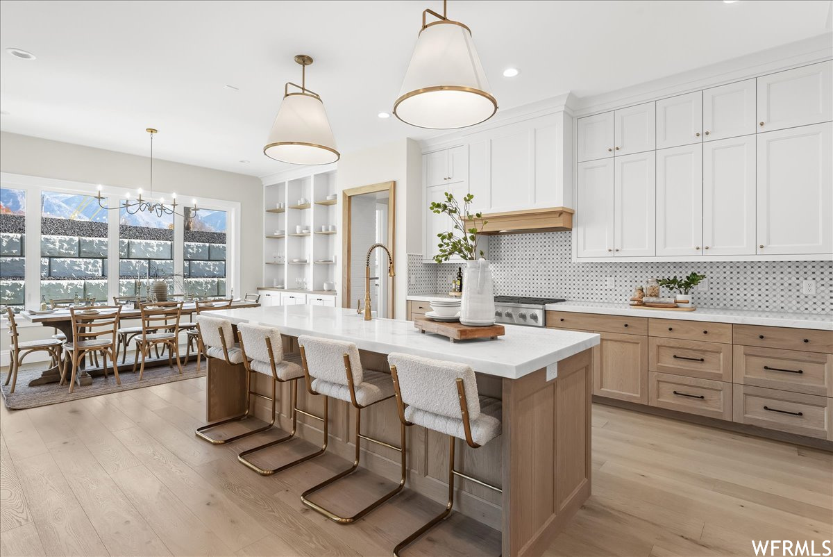 Kitchen with a chandelier, a center island with sink, pendant lighting, light wood-type flooring, and backsplash