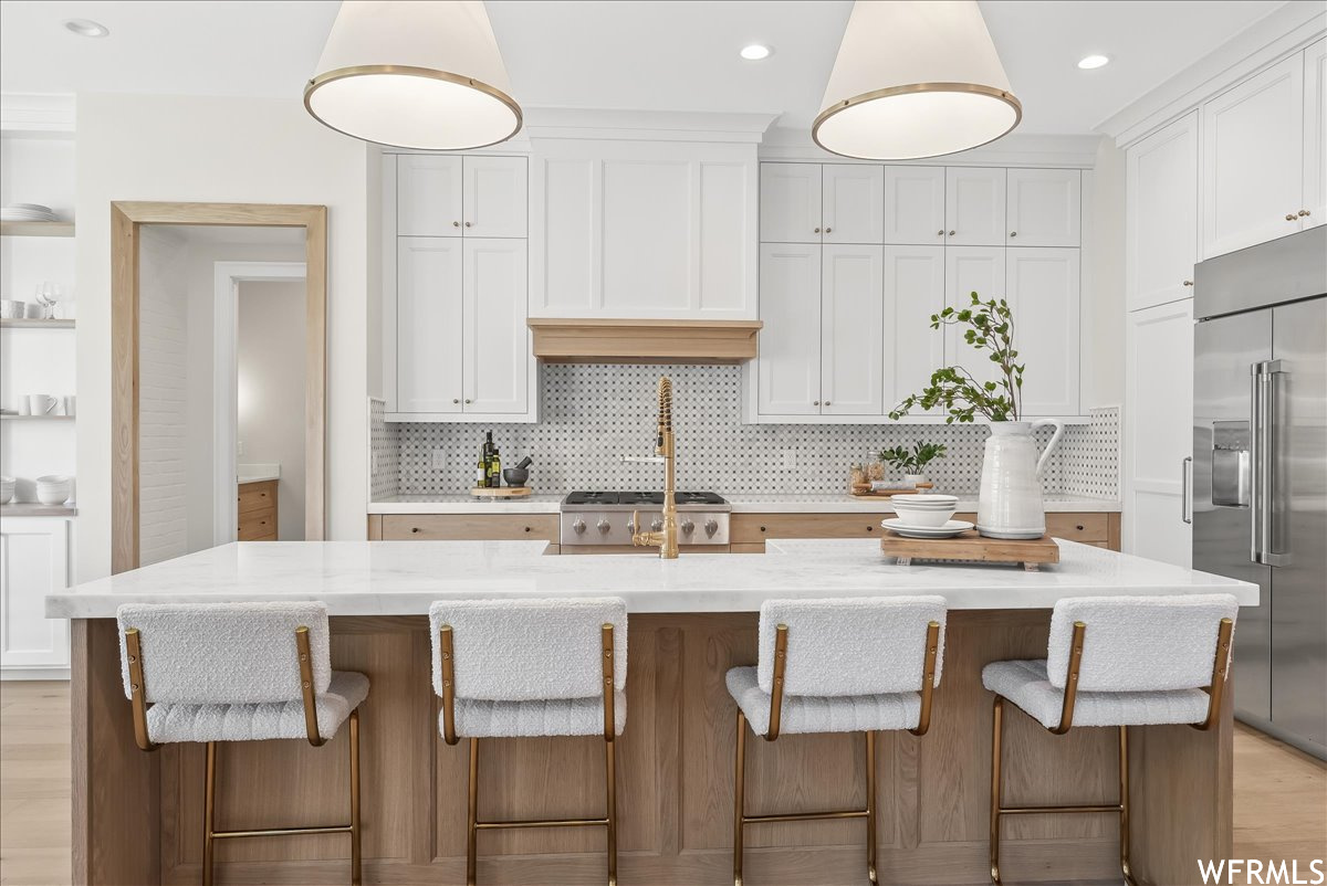 Kitchen featuring tasteful backsplash, light hardwood / wood-style floors, built in fridge, and a kitchen island with sink