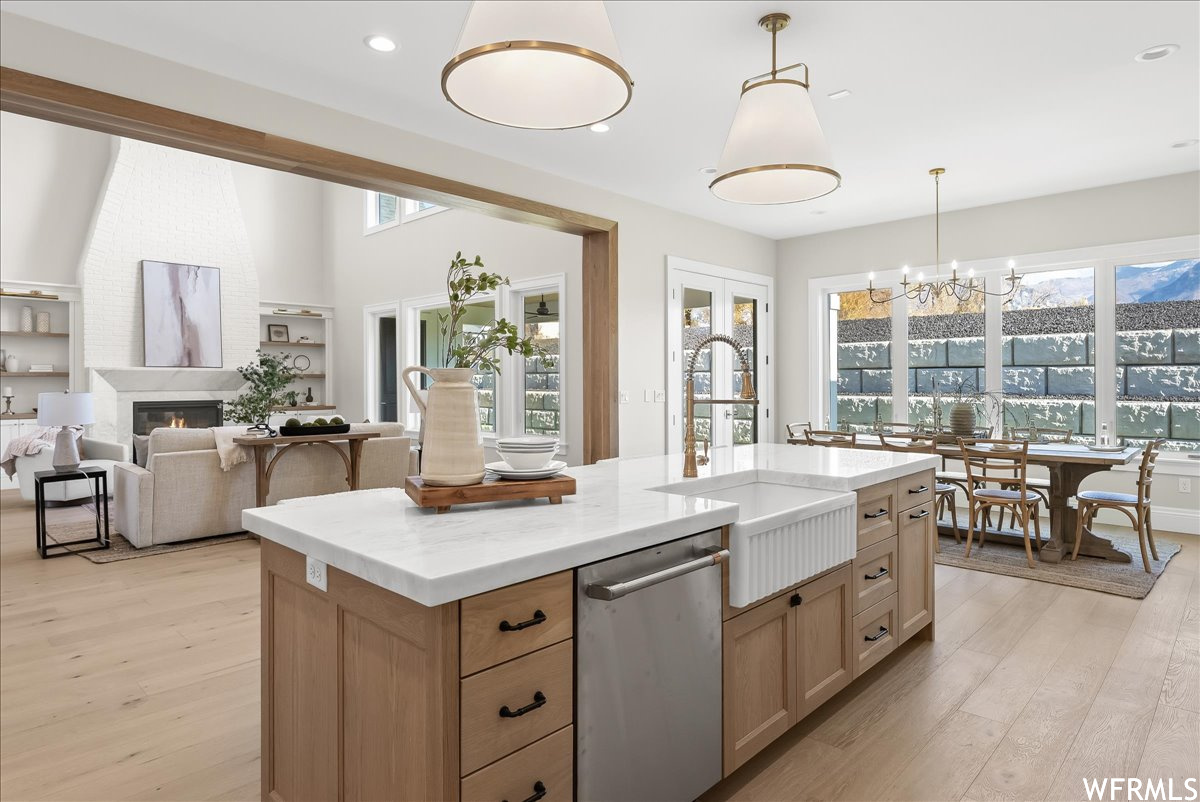 Kitchen featuring pendant lighting, a center island with sink, dishwasher, and light hardwood / wood-style floors