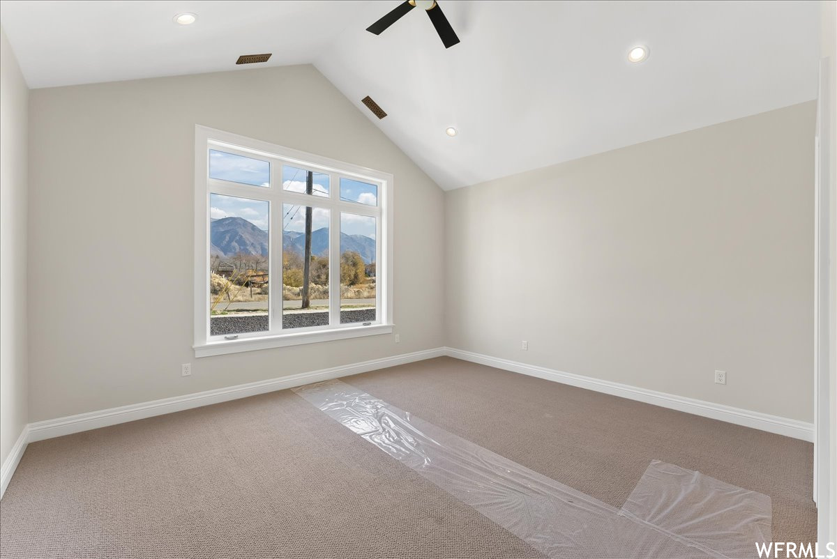 Unfurnished room featuring light colored carpet, ceiling fan, a mountain view, and vaulted ceiling