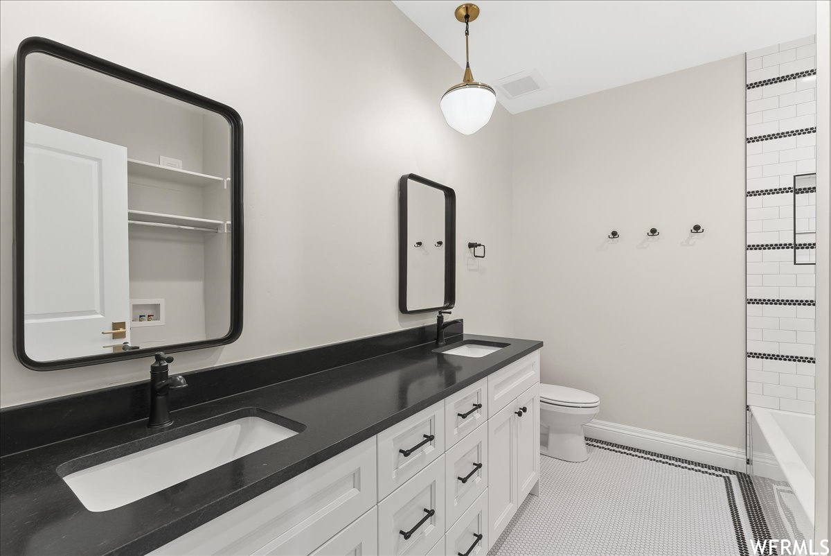 Full bathroom featuring tiled shower / bath, tile floors, dual bowl vanity, and toilet