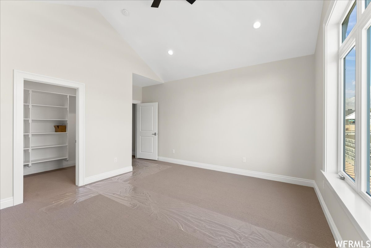 Unfurnished bedroom featuring light carpet, a closet, high vaulted ceiling, ceiling fan, and a spacious closet