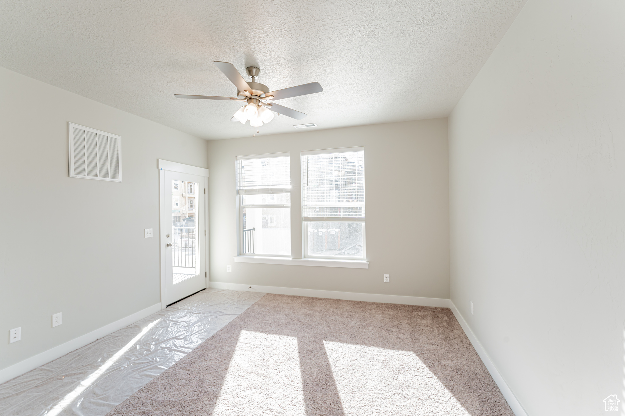 Carpeted empty room with a healthy amount of sunlight, a textured ceiling, and ceiling fan