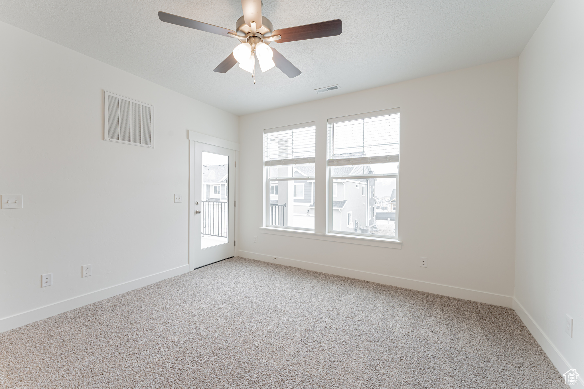 Empty room featuring light carpet, ceiling fan, and a wealth of natural light