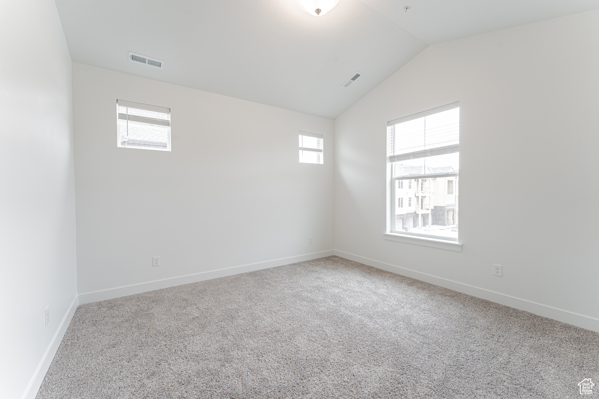 Carpeted spare room with plenty of natural light and vaulted ceiling