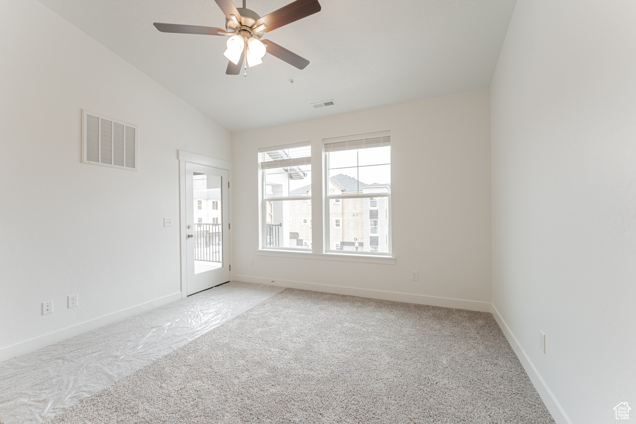 Carpeted empty room featuring vaulted ceiling, a healthy amount of sunlight, and ceiling fan
