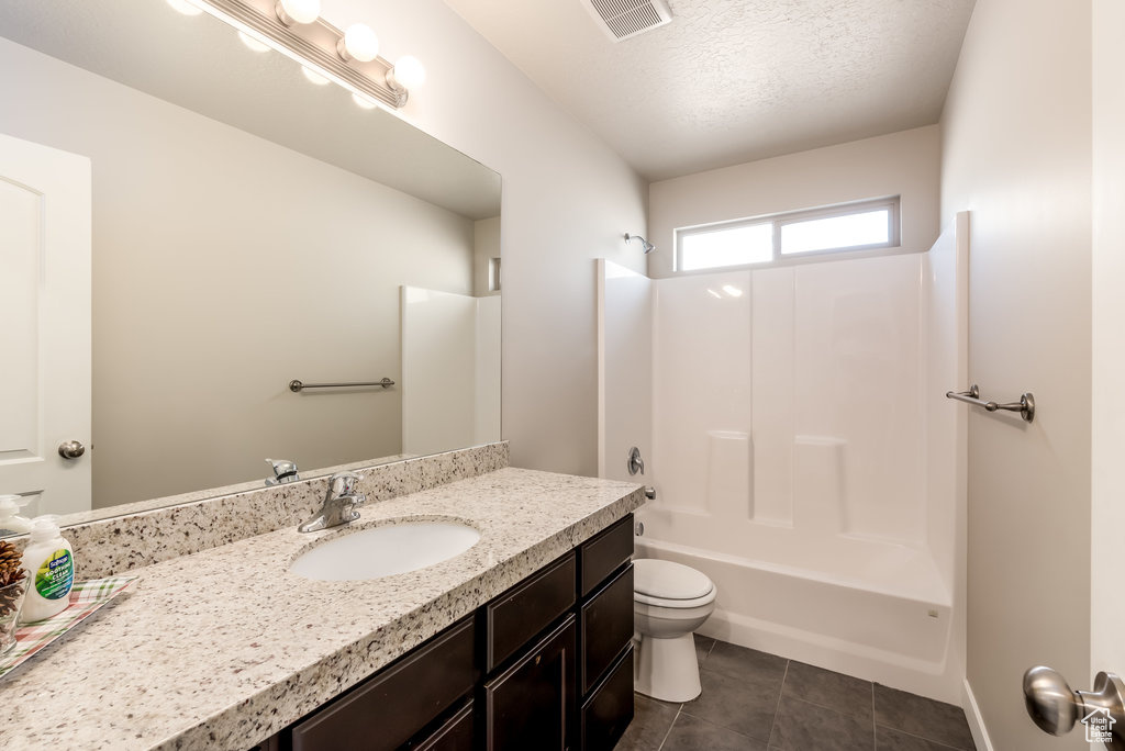 Full bathroom with toilet, large vanity, tile floors, washtub / shower combination, and a textured ceiling