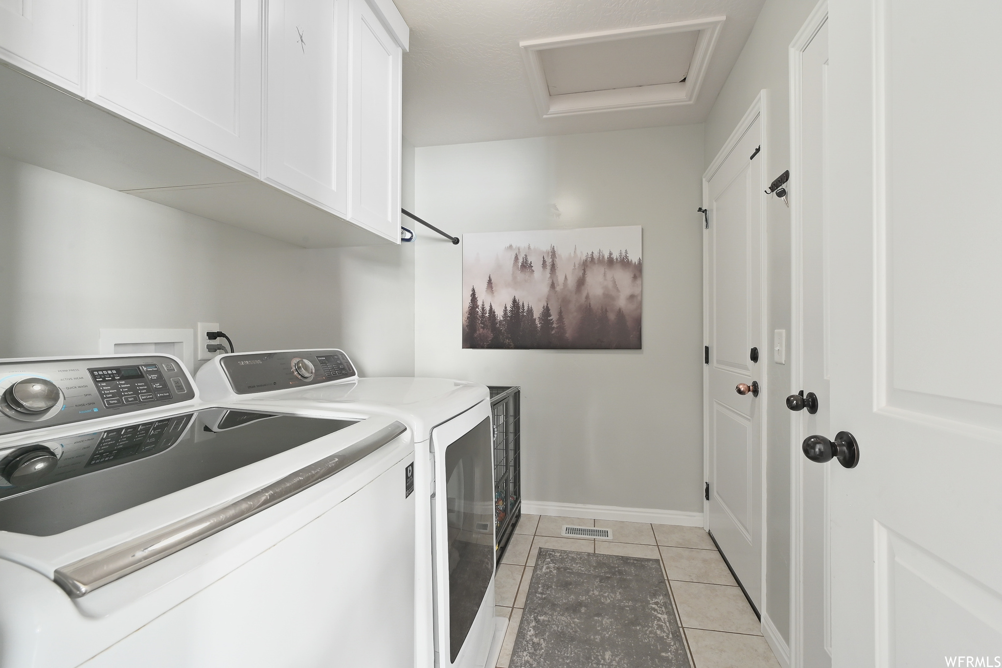 Washroom featuring washer and dryer, cabinets, and light tile floors