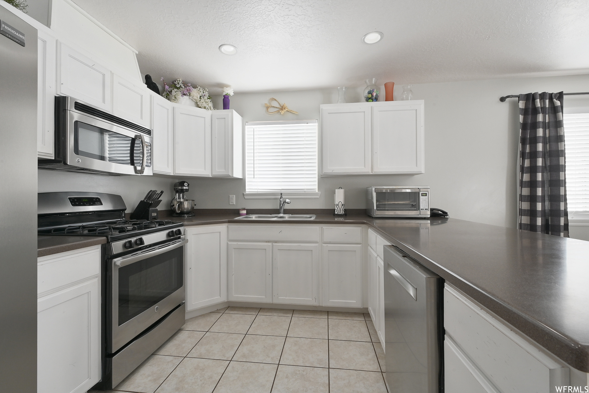 Kitchen featuring light tile floors, sink, stainless steel appliances, and white cabinetry