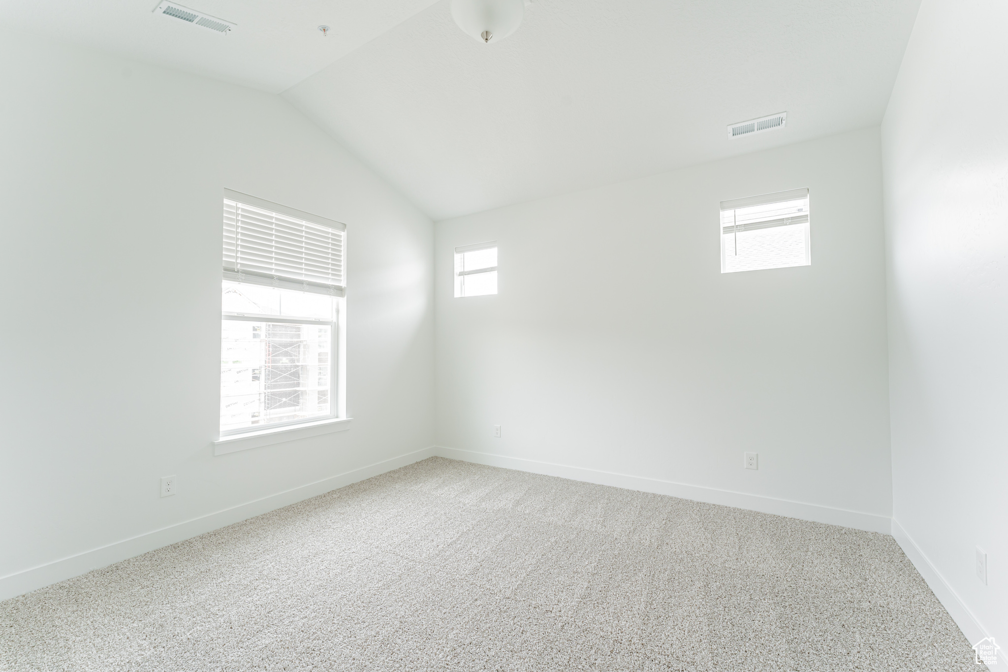Empty room featuring plenty of natural light, lofted ceiling, and light carpet