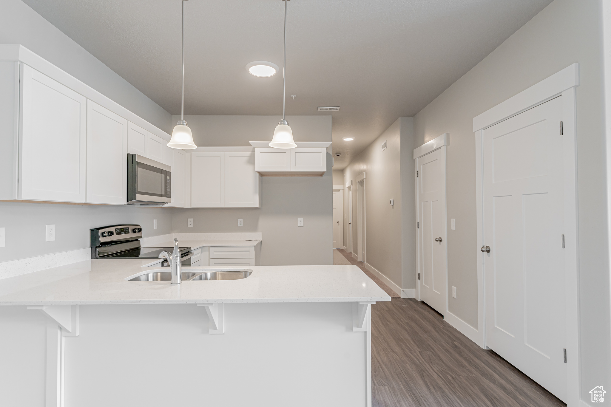 Kitchen featuring stainless steel appliances, decorative light fixtures, wood-type flooring, white cabinetry, and sink