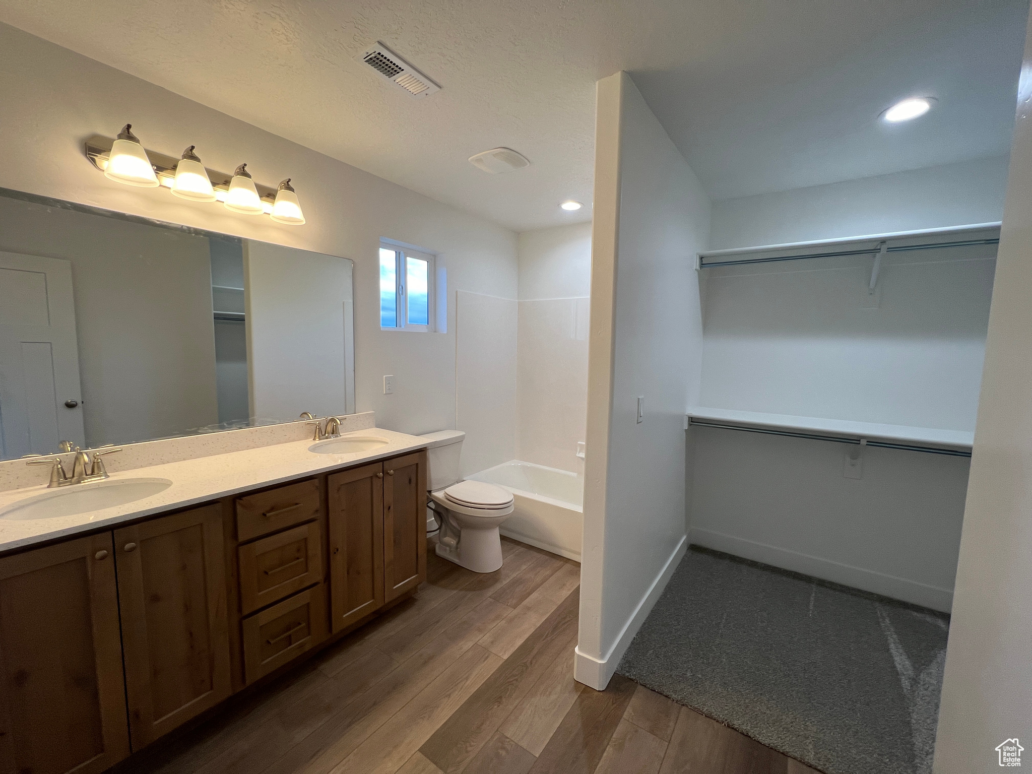 Full master bathroom with toilet, dual sinks, wood-type flooring, oversized vanity, and shower / tub combination