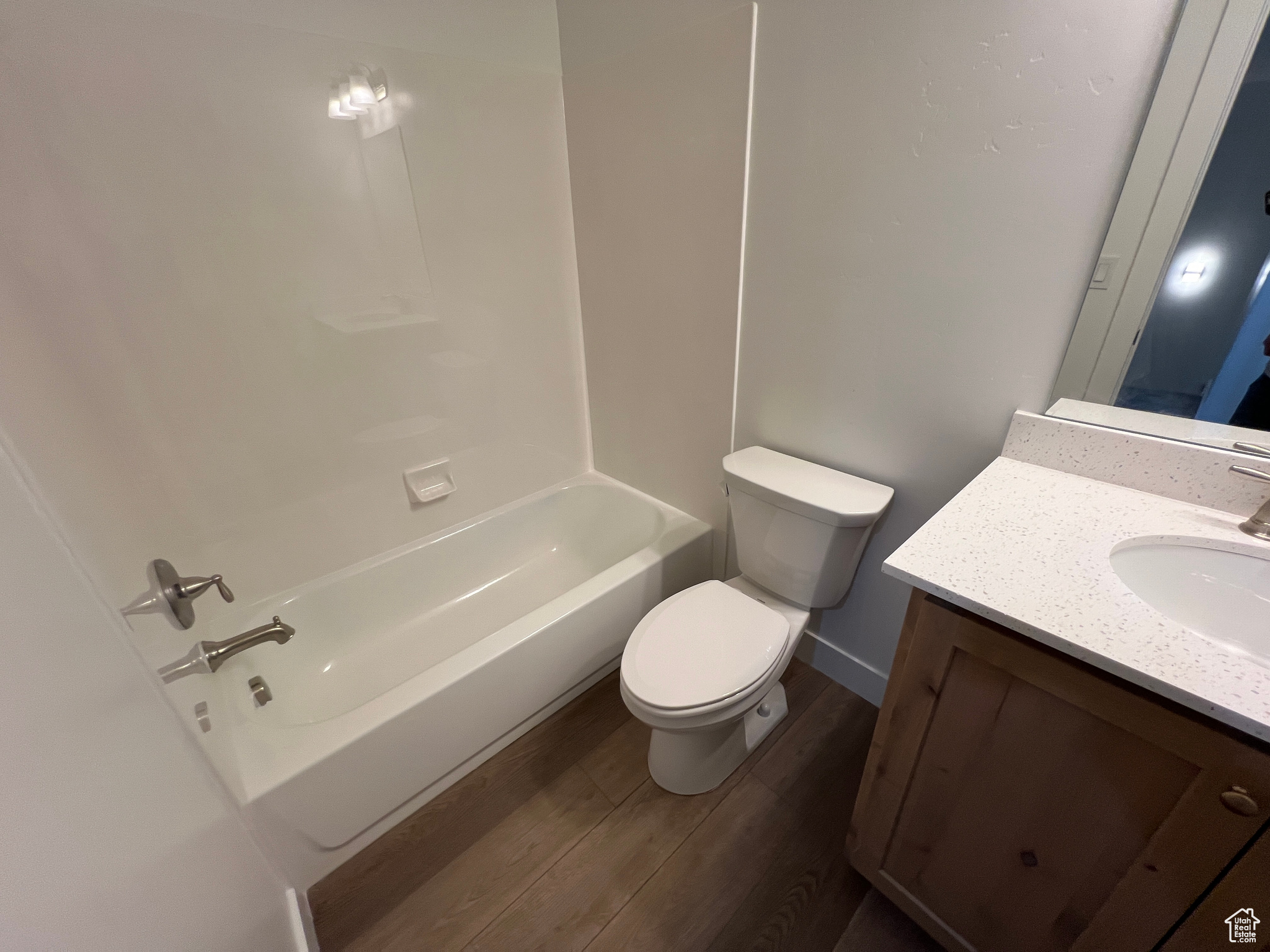 Full bathroom with washtub / shower combination, toilet, hardwood / wood-style flooring, and vanity