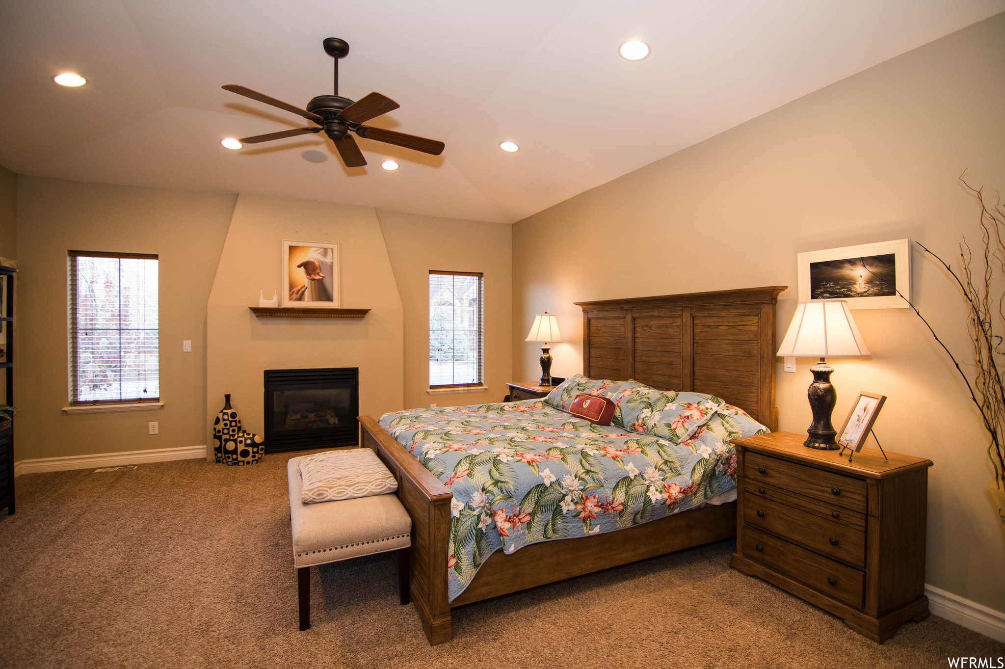Carpeted bedroom with multiple windows, ceiling fan, and vaulted ceiling