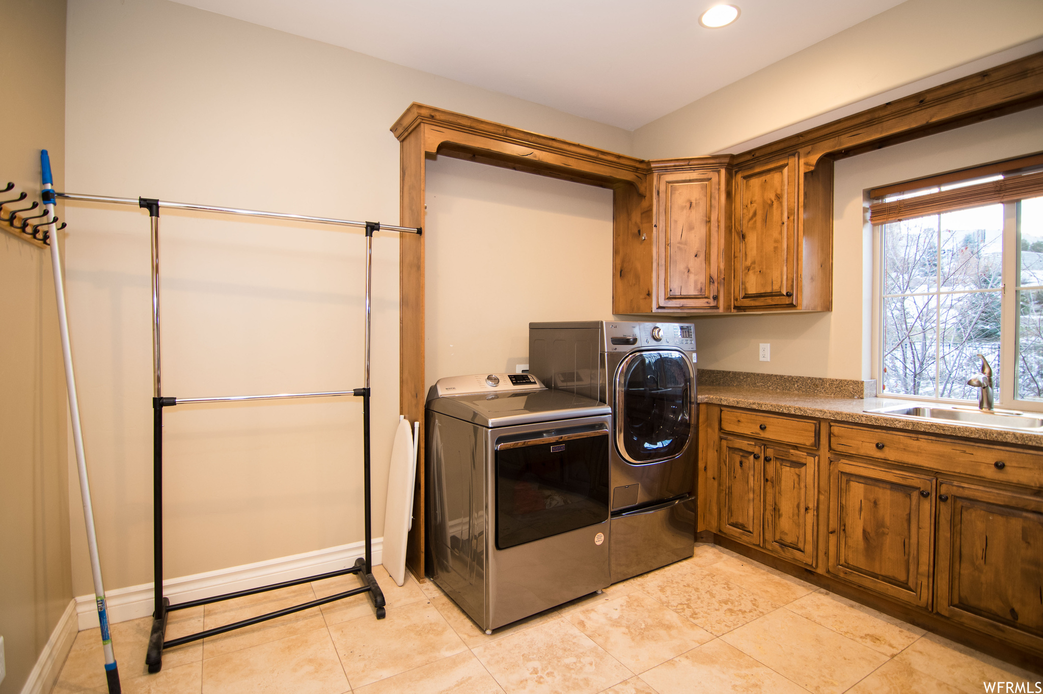 Clothes washing area with independent washer and dryer, cabinets, sink, and light tile floors