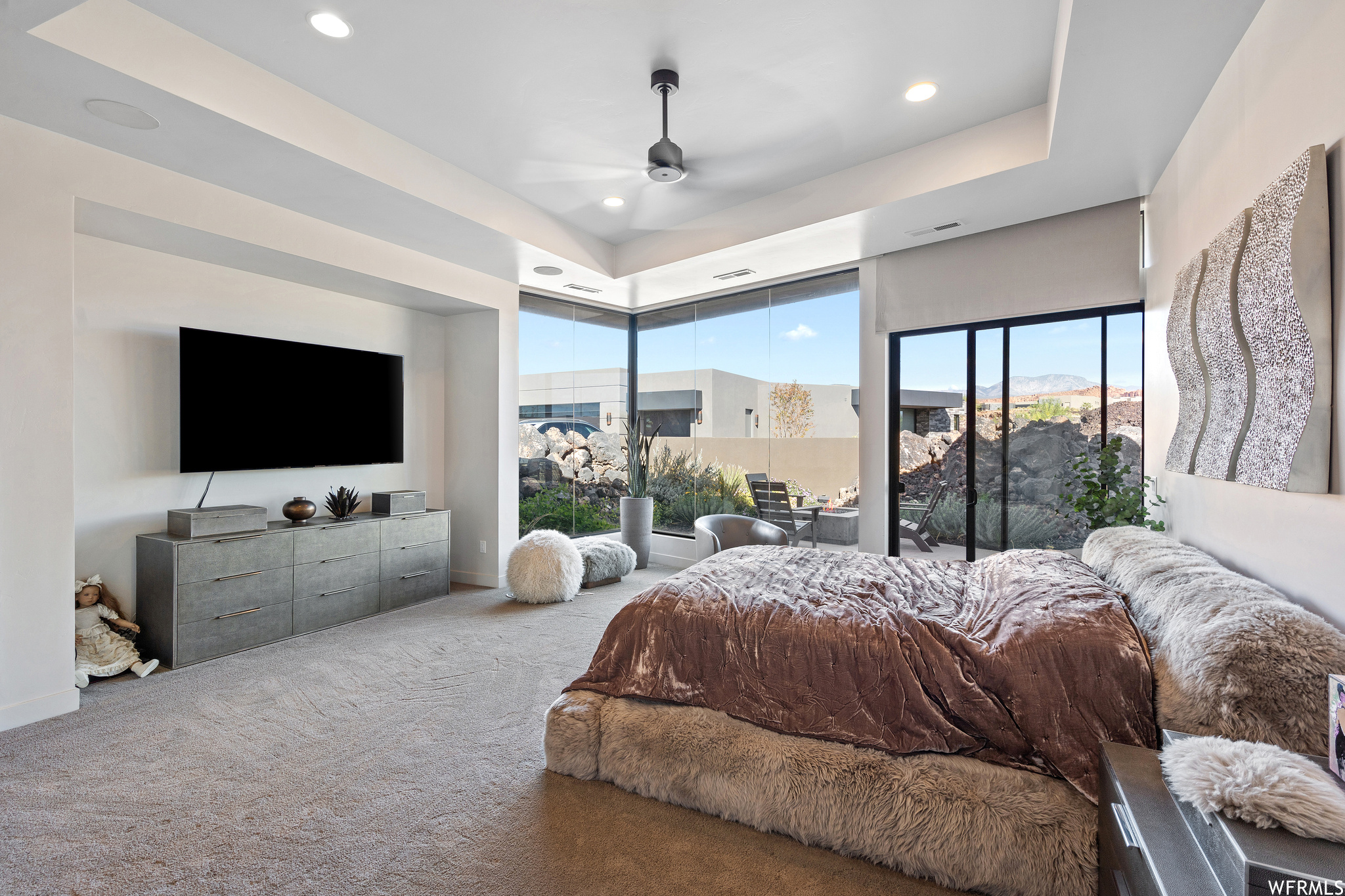 Bedroom with light colored carpet, ceiling fan, and a tray ceiling