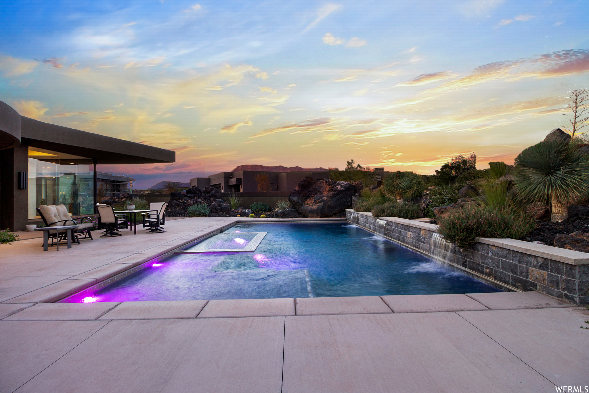Pool at dusk featuring pool water feature and a patio