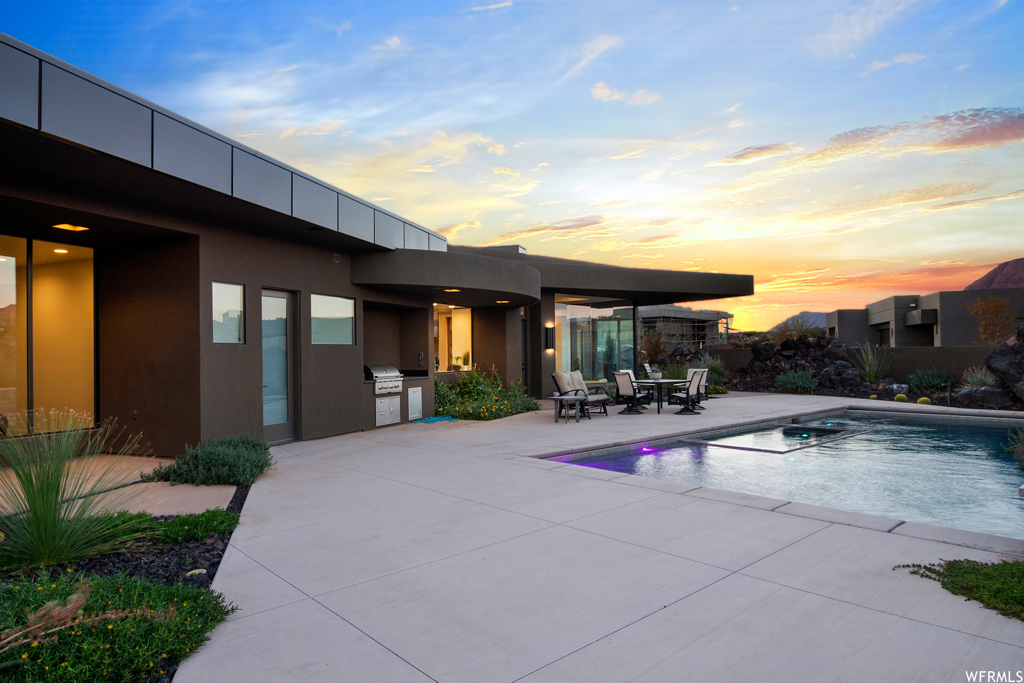 Pool at dusk featuring a patio, exterior kitchen, and a grill