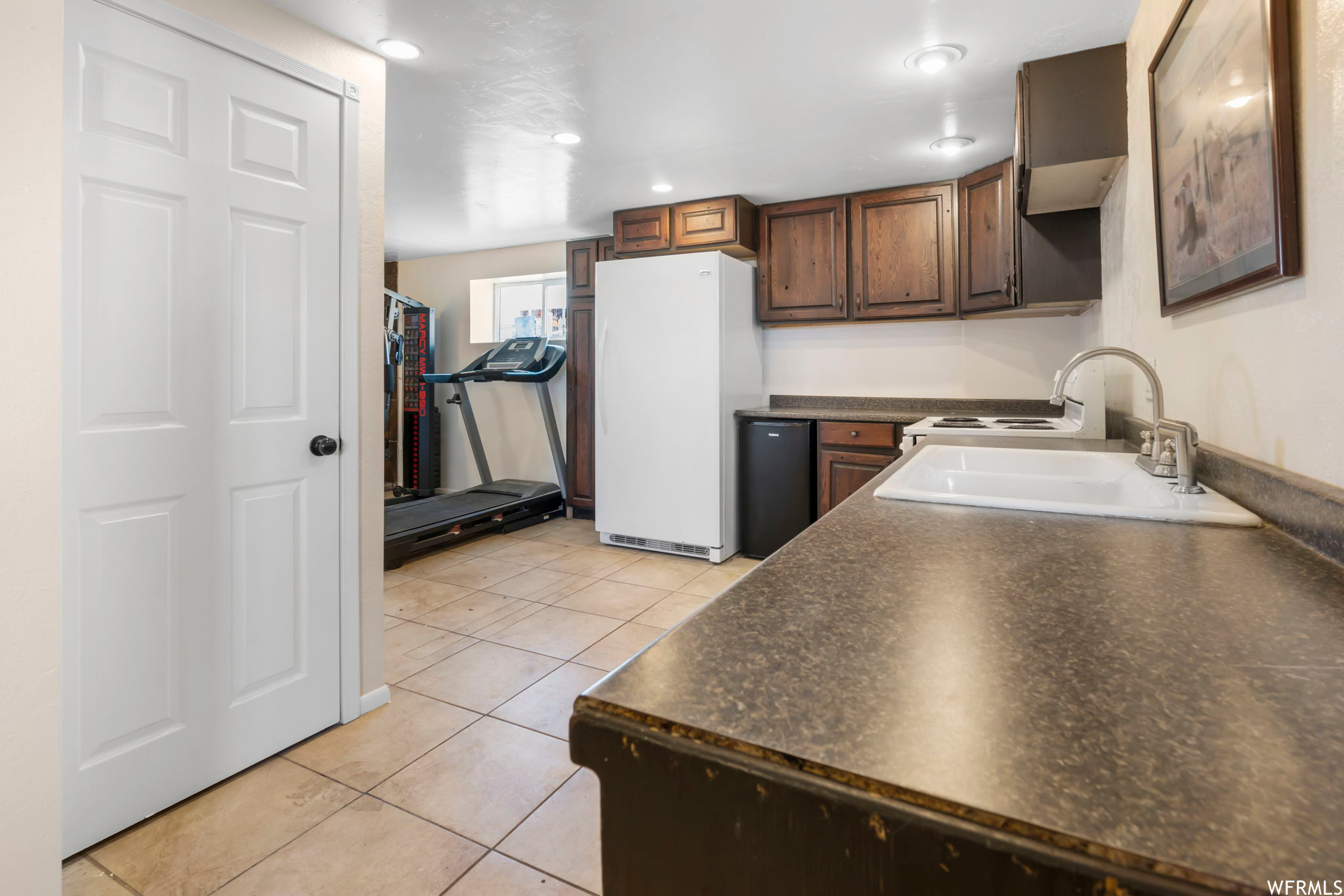 Kitchen featuring sink, white refrigerator, dark brown cabinetry, black dishwasher, and light tile floors