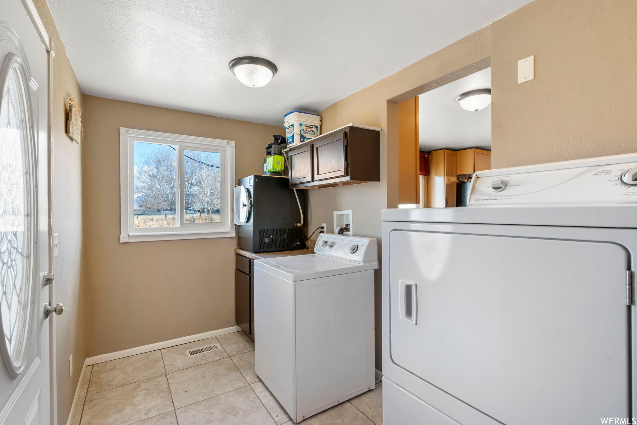 Clothes washing area with washing machine and clothes dryer, cabinets, and light tile floors