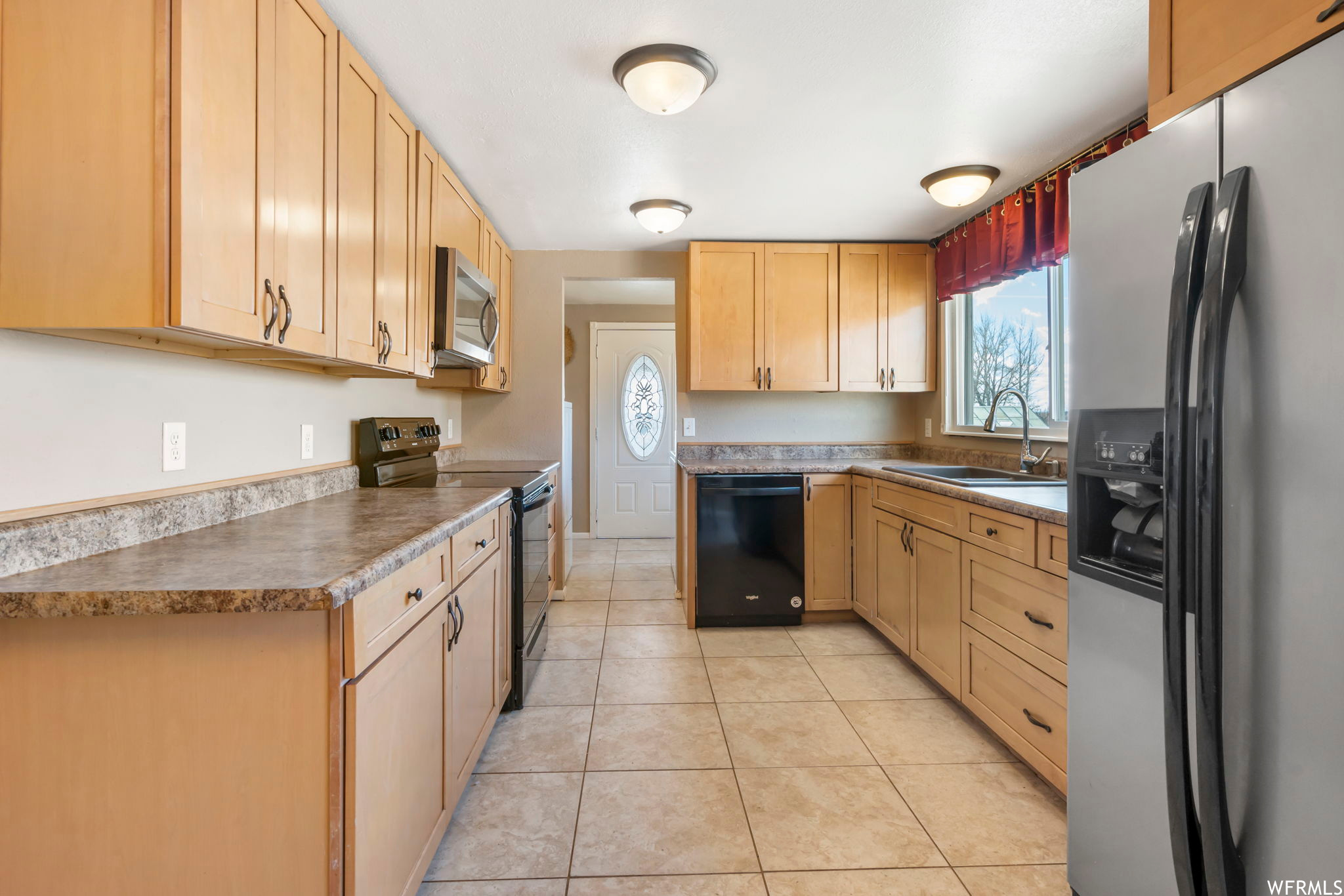 Kitchen with light tile floors, black appliances, sink, and light brown cabinetry