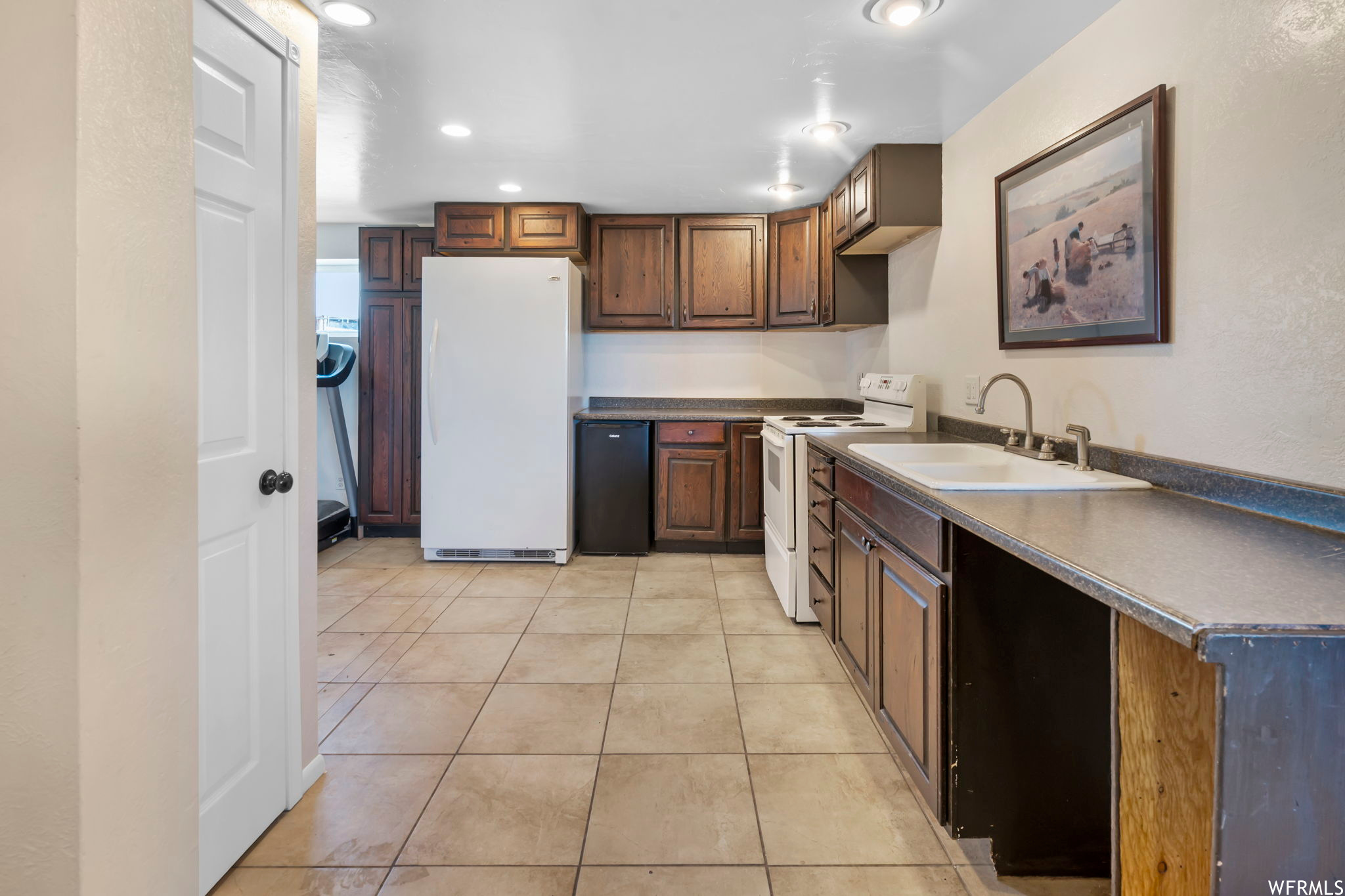 Kitchen with light tile floors, sink, and white appliances