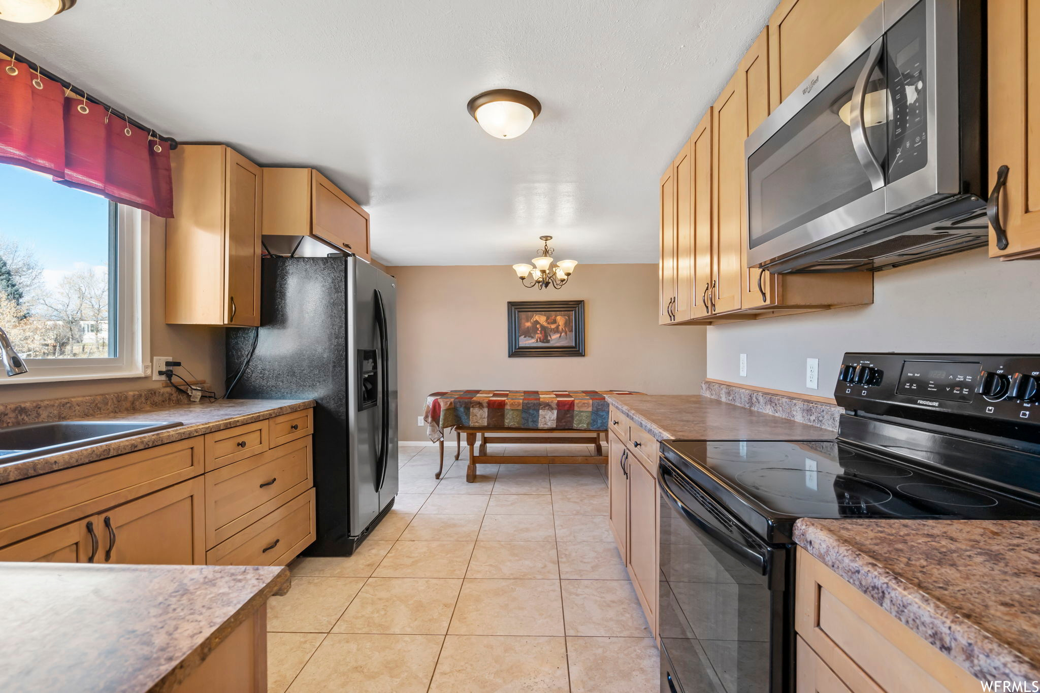 Kitchen featuring light tile floors, sink, a chandelier, hanging light fixtures, and stainless steel appliances