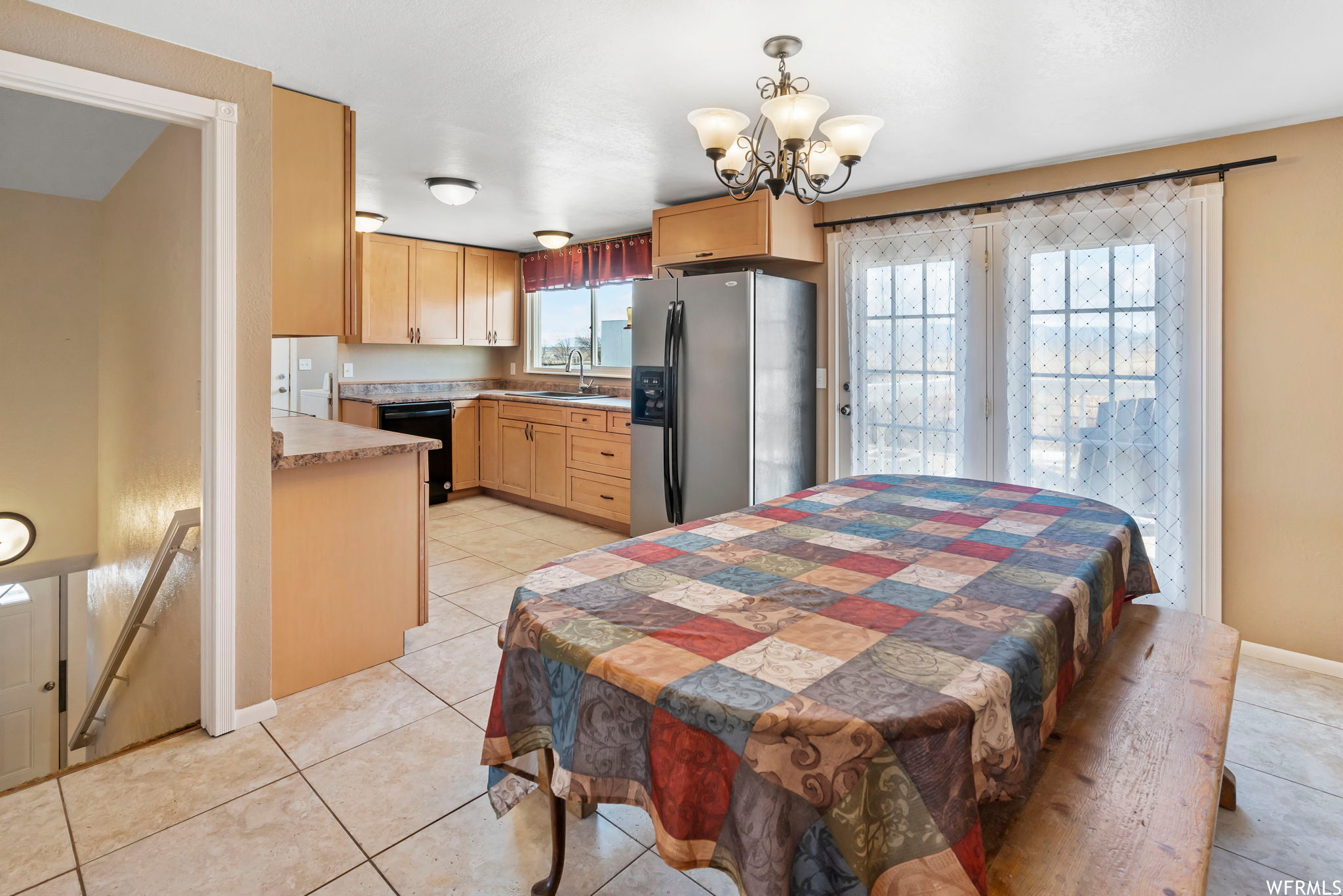 Interior space with multiple windows, stainless steel refrigerator with ice dispenser, light tile flooring, and a chandelier