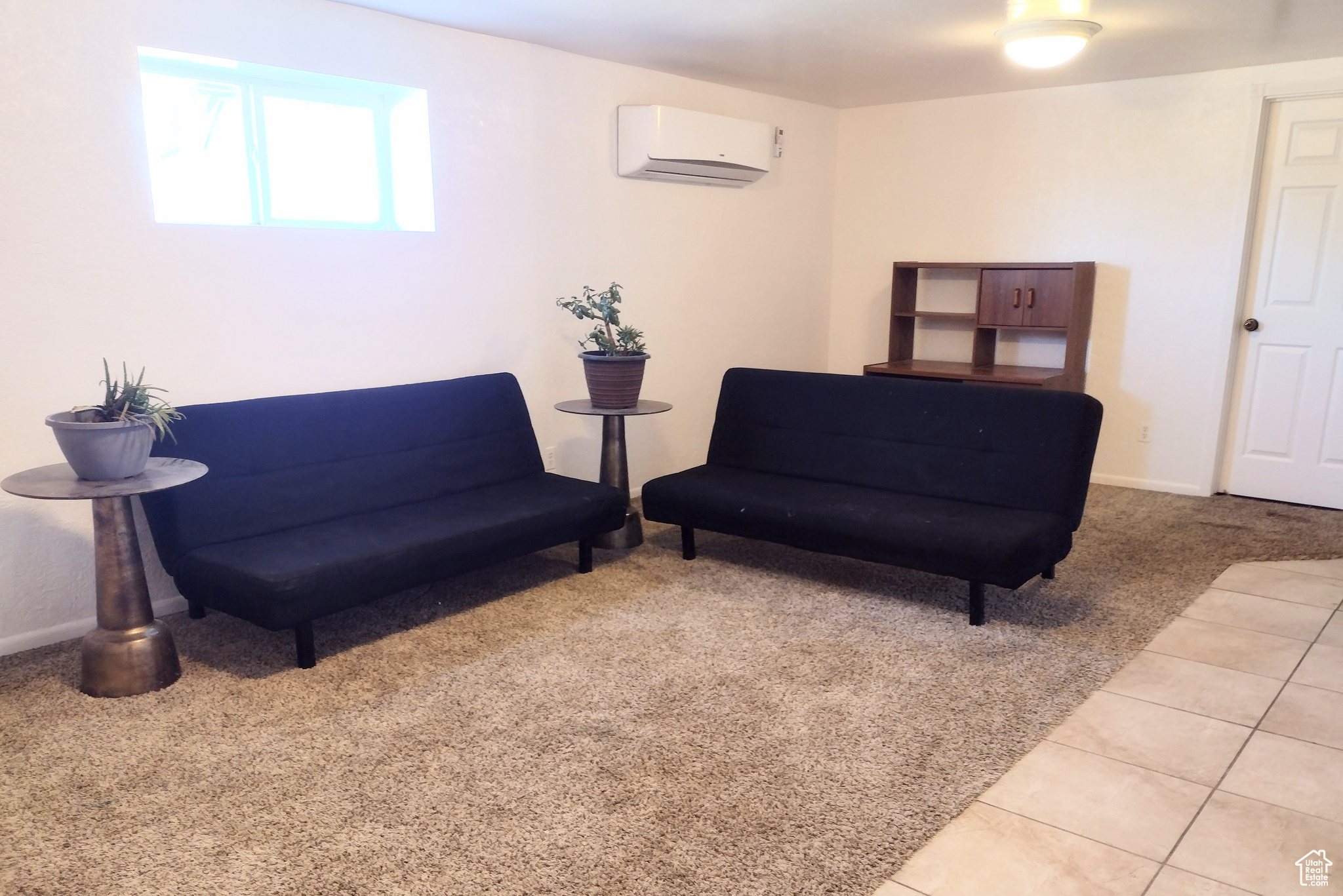 Living area with light tile flooring and an AC wall unit