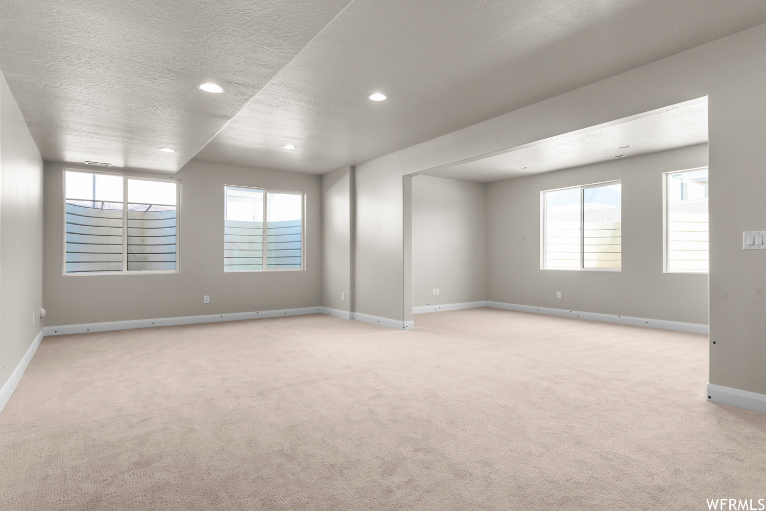 Spare room featuring light colored carpet, a textured ceiling, and a wealth of natural light