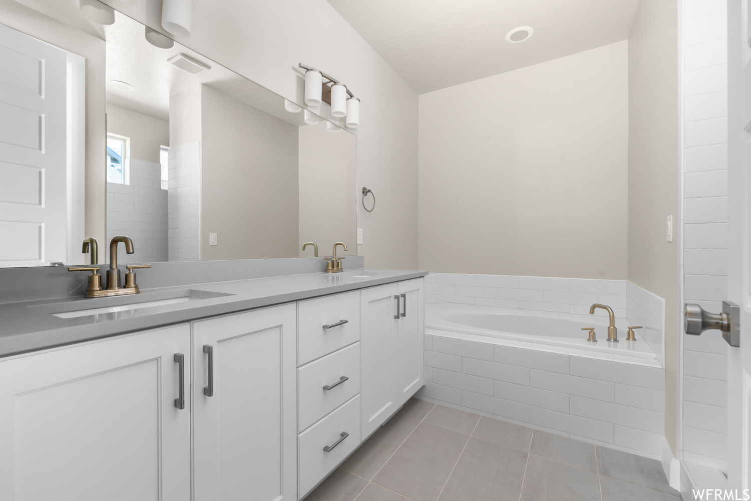 Bathroom featuring tile floors, tiled tub, and double sink vanity