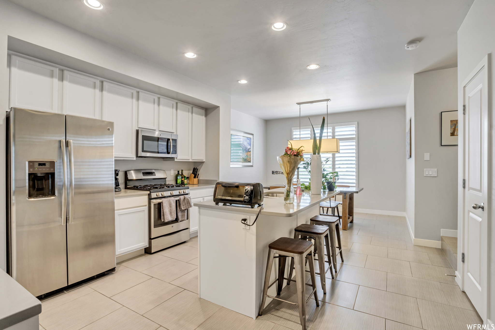 Kitchen with hanging light fixtures, appliances with stainless steel finishes, a breakfast bar area, white cabinets, and a center island with sink