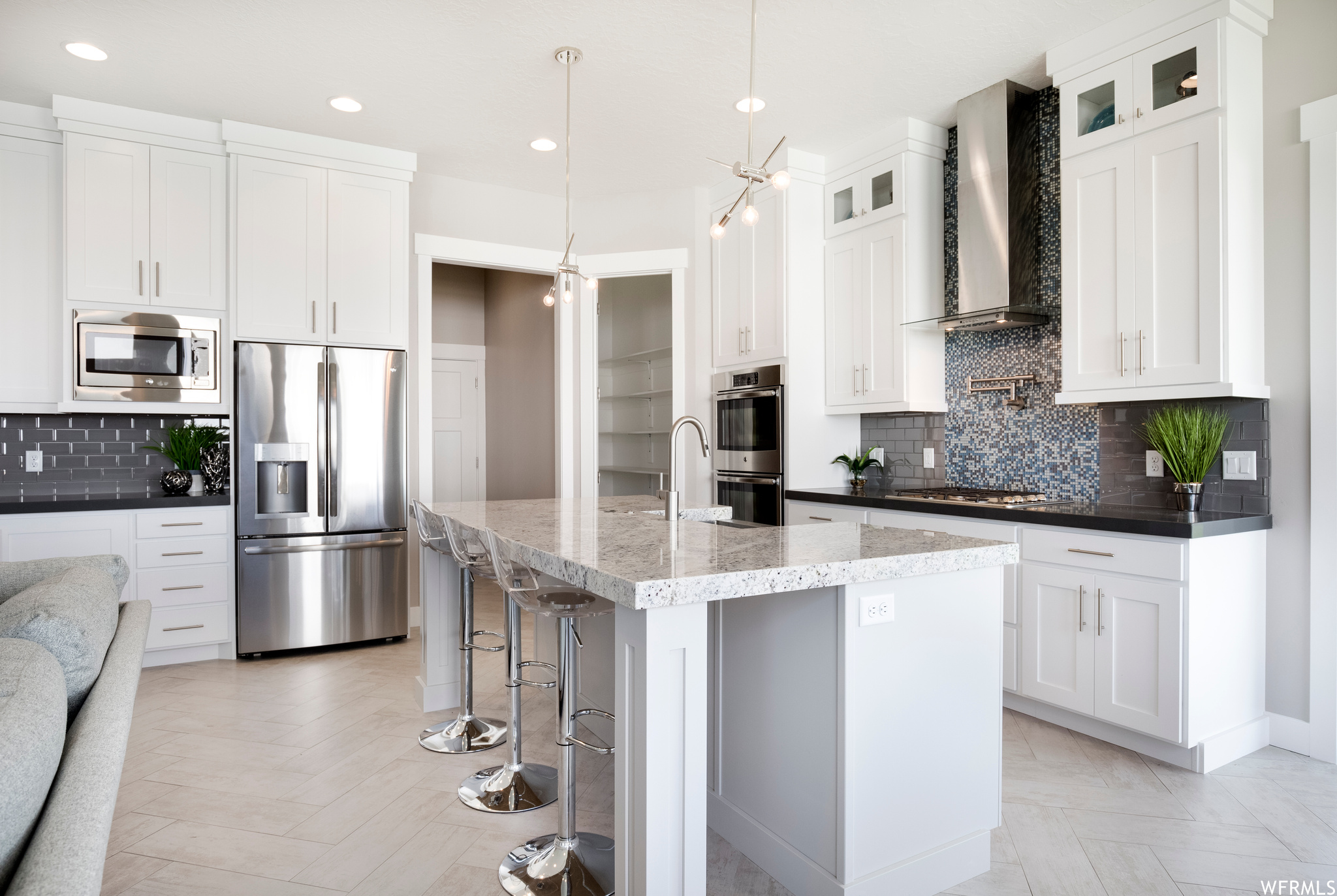 Kitchen featuring appliances with stainless steel finishes, wall chimney range hood, pendant lighting, white cabinets, and backsplash