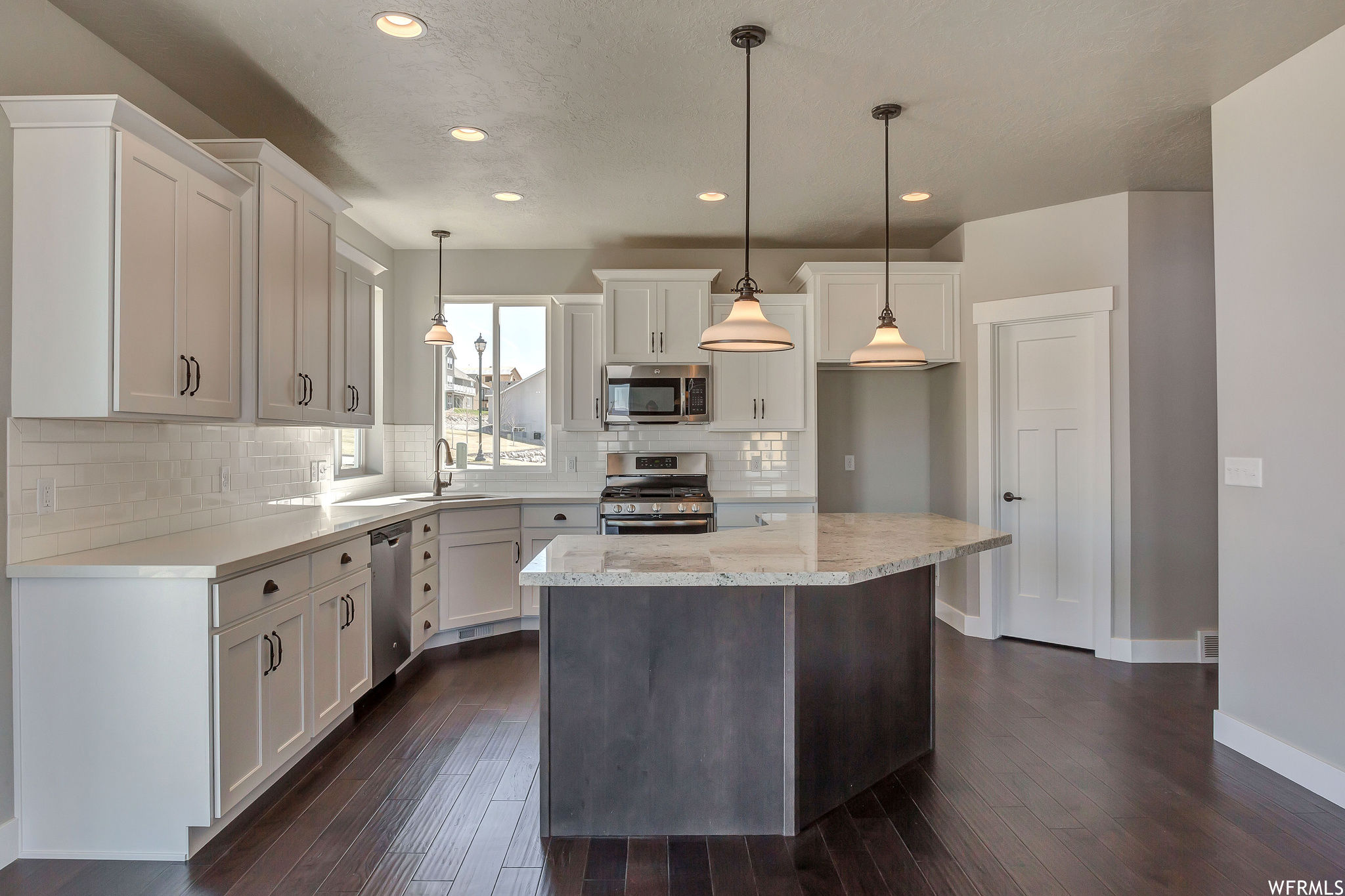 Kitchen with white cabinets, appliances with stainless steel finishes, tasteful backsplash, and pendant lighting