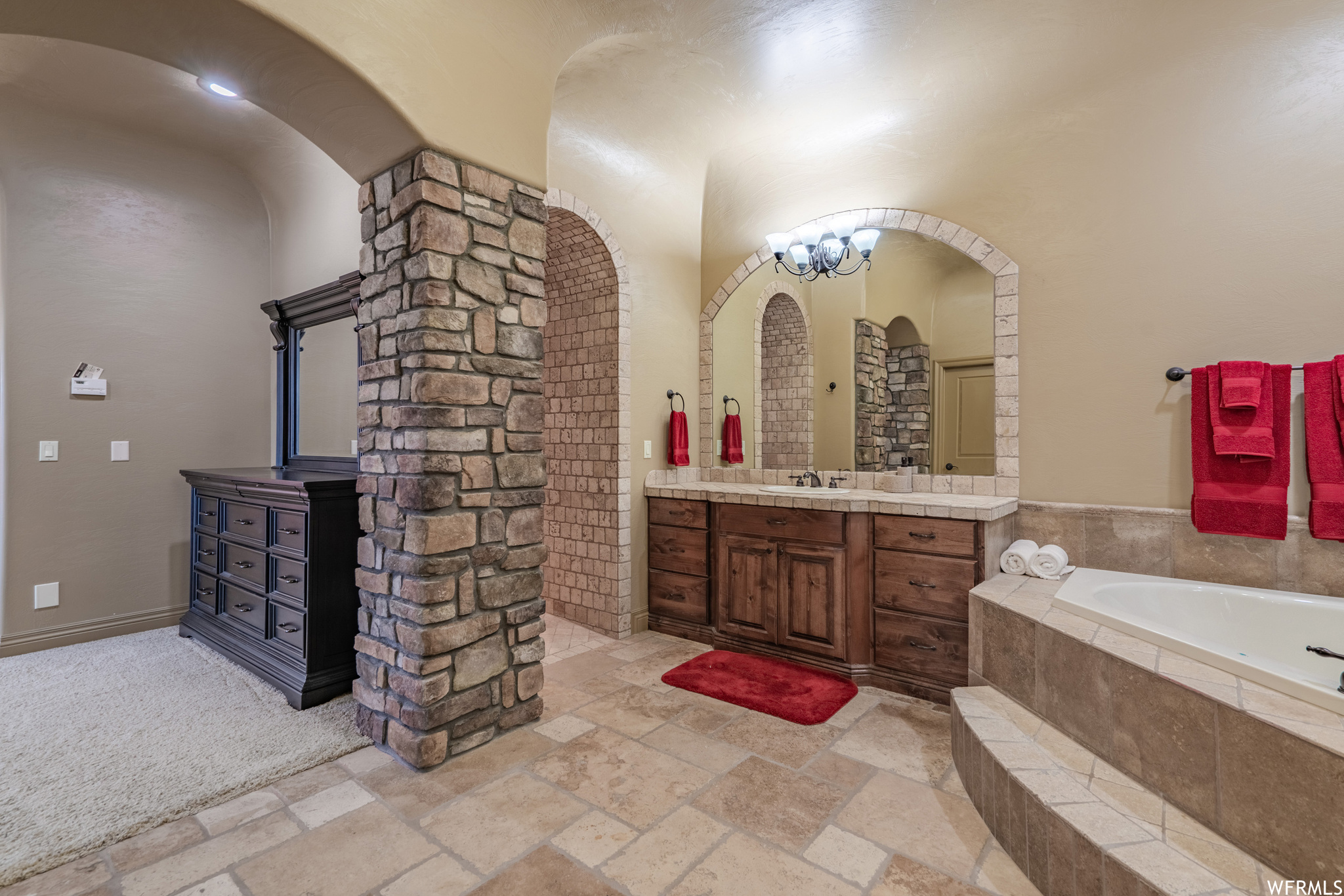 Master Bathroom with tile flooring, tiled tub, a chandelier, and vanity with extensive cabinet space