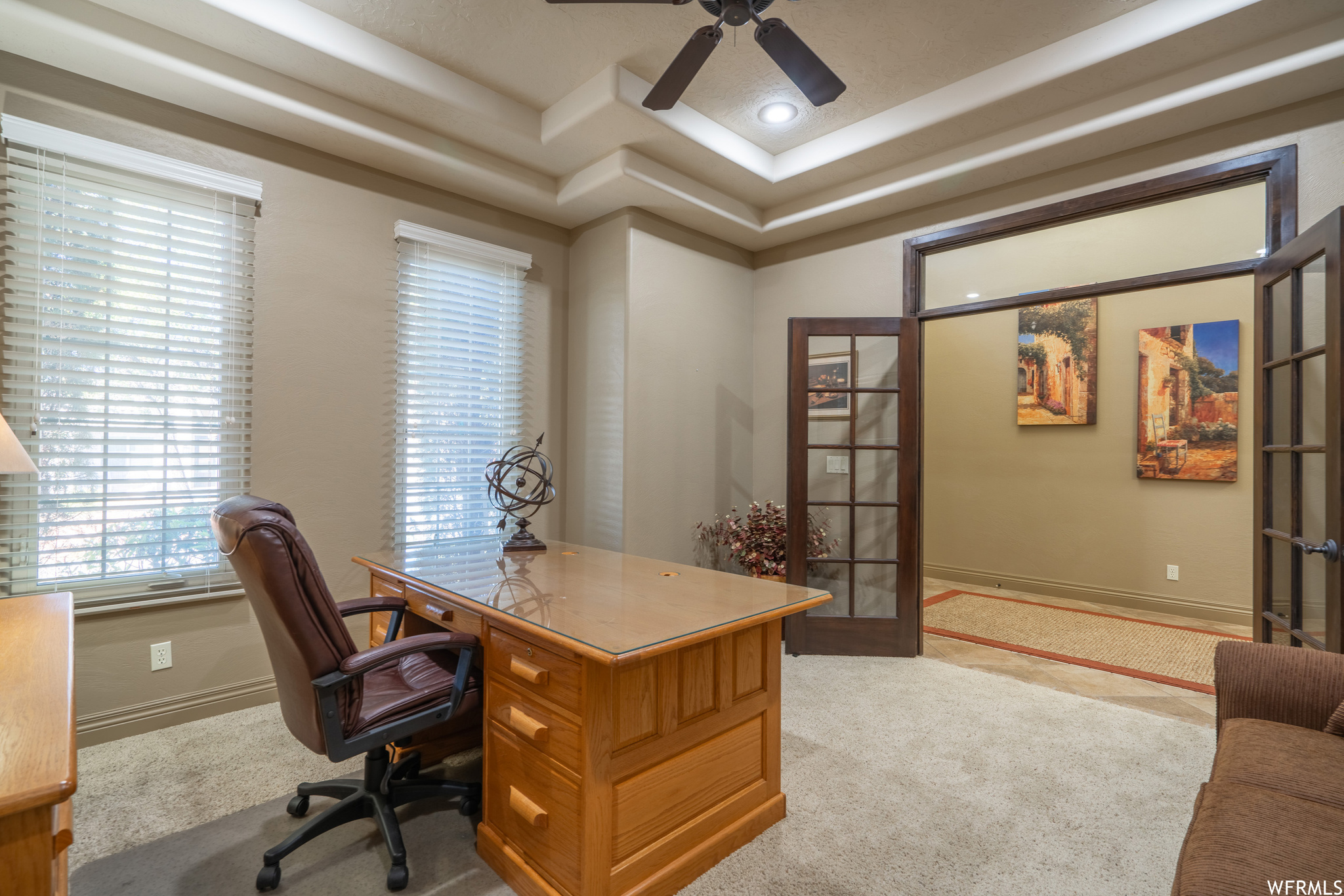 Office space with a raised ceiling, light carpet, and ceiling fan