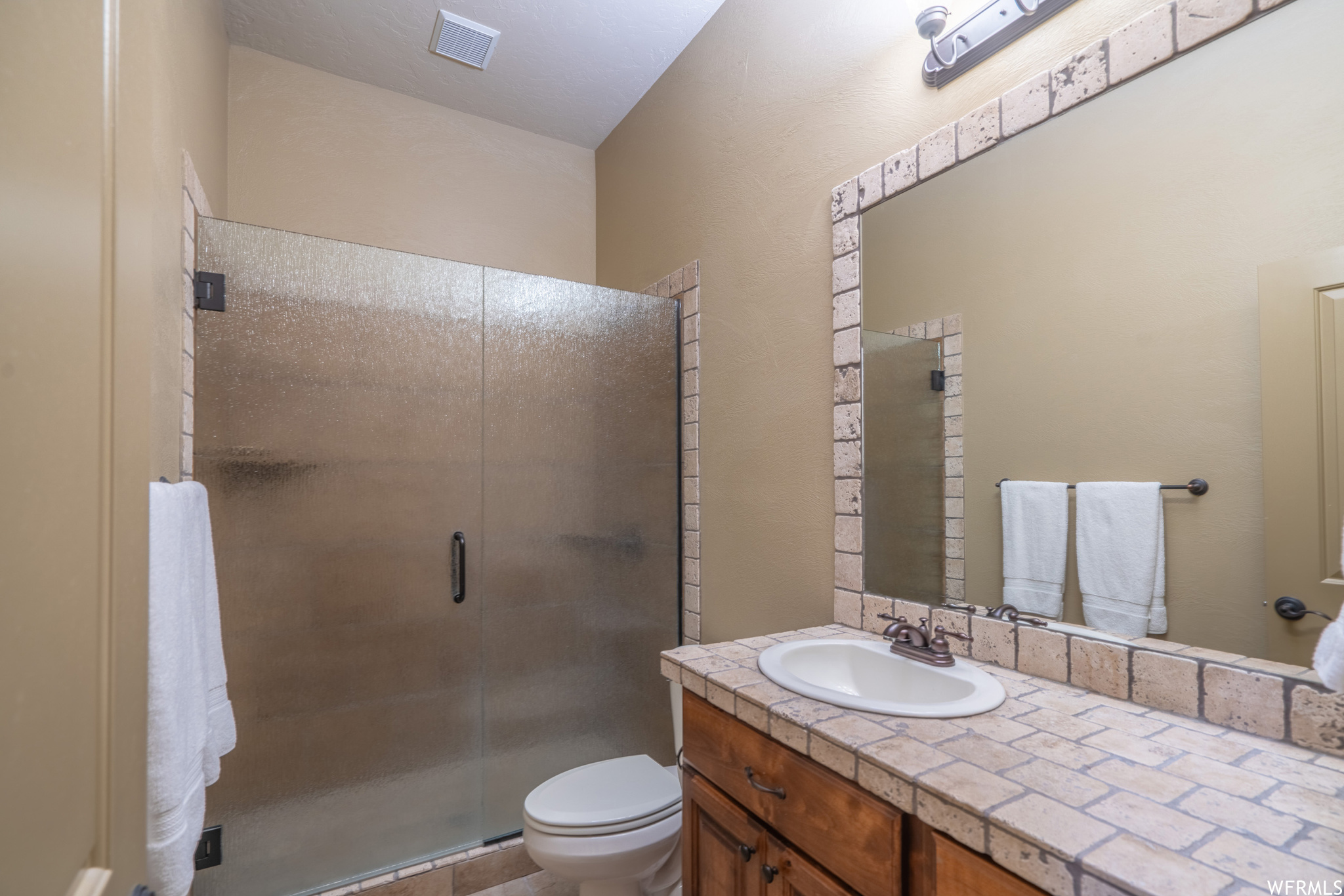 Bathroom with toilet, a shower with door, and vanity