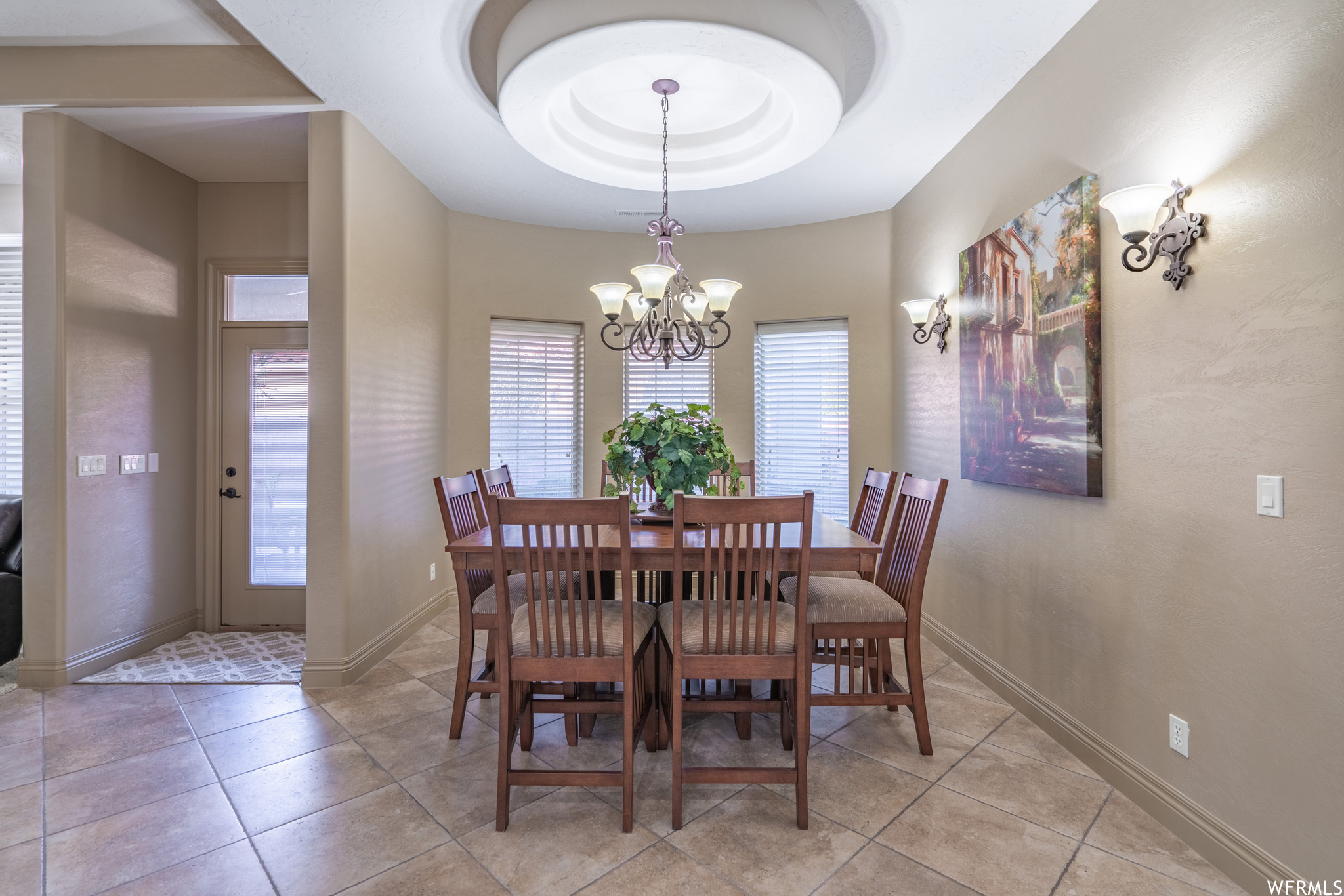 Dining area with a raised ceiling, an inviting chandelier, and light tile flooring