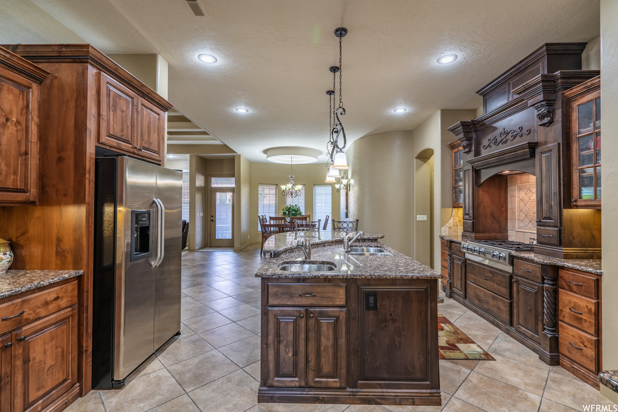 Kitchen with sink, pendant lighting, dark stone countertops, stainless steel appliances, and a center island with sink