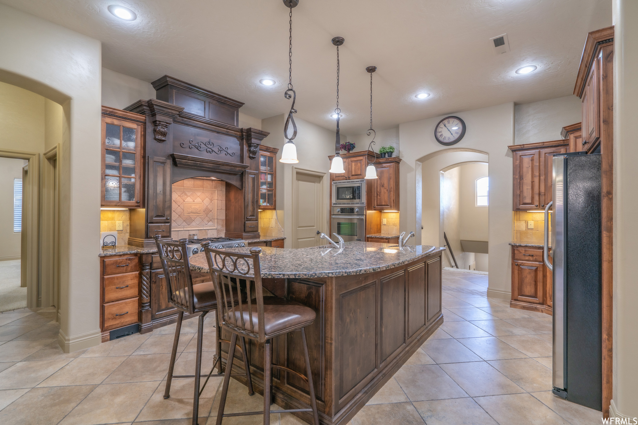 Kitchen with hanging light fixtures, a kitchen island with sink, tasteful backsplash, stainless steel appliances, and light tile floors